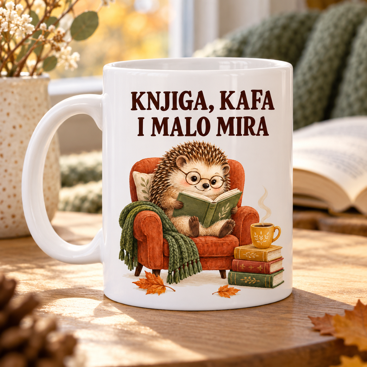 Bela šolja sa natpisom Knjiga, kafa i malo mira i ilustracijom ježa koji čita u fotelji